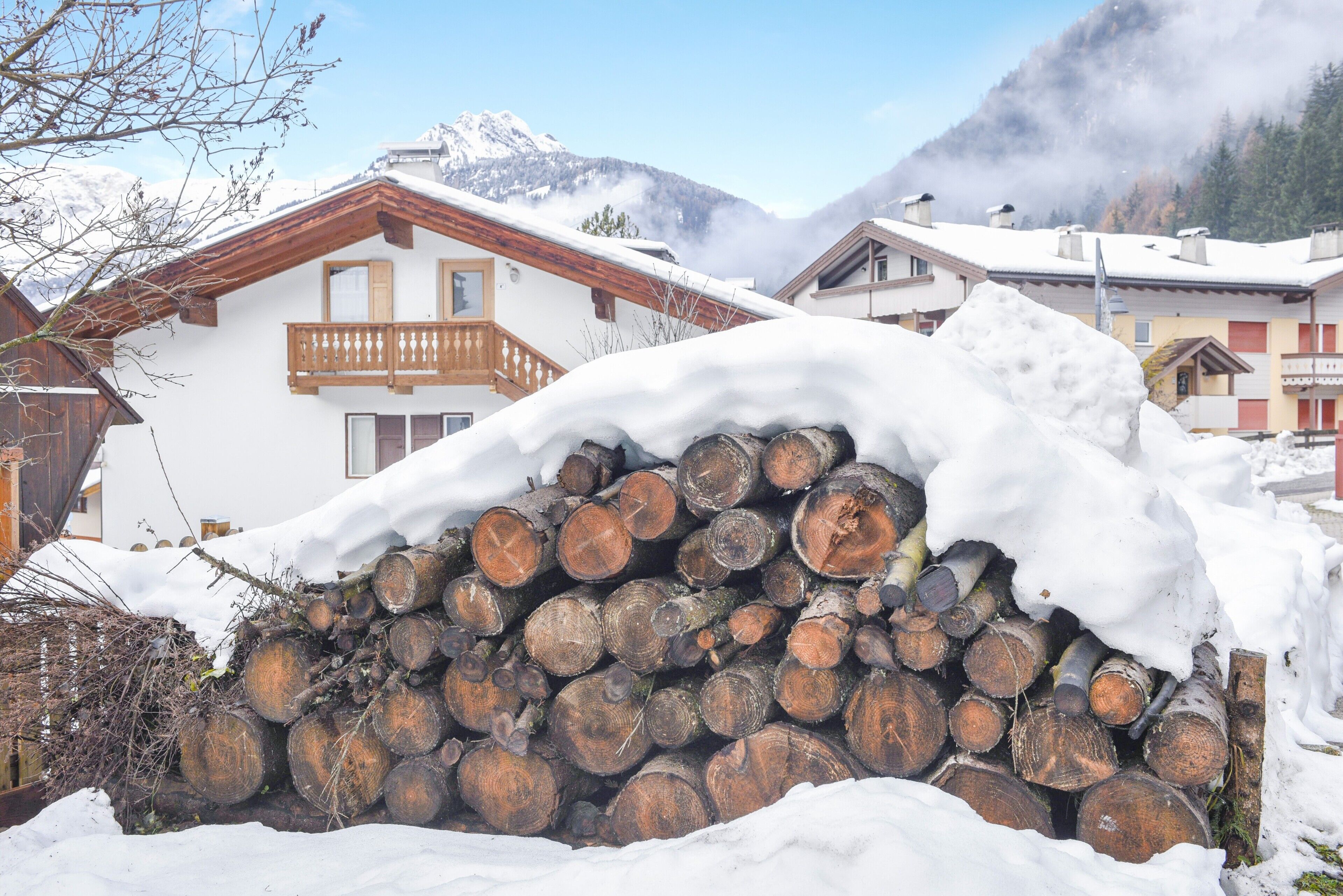 Un montón de troncos nevados frente a un edificio con balcón.