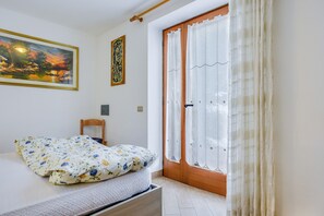 Une chambre à coucher avec un lit, une chaise en bois, une porte avec des rideaux et un tableau accroché au mur.
