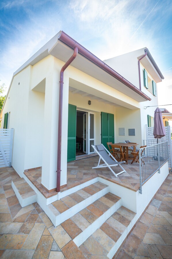 A house with a covered patio, a dining area, and a staircase leading to the entrance.