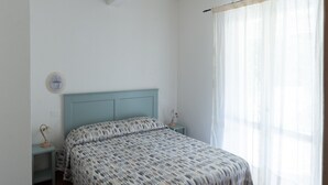 A bedroom with a bed, a nightstand, a wall clock, and a window with curtains. - Holiday Home 'Il Timo' with Sea View, Wi-Fi and Air Conditioning (Marciana)