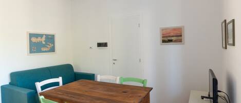 A dining area with a wooden table, green chairs, a teal sofa, and a white cabinet with a monitor.