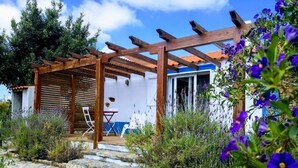 A rustic outdoor seating area with a wooden pergola, stone steps, and a white building with a blue door.