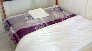 A bed with a white and purple floral bedspread, a white pillow, and a wooden headboard.