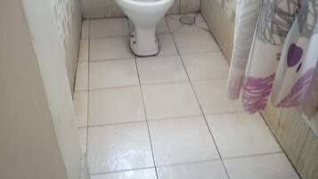 A small bathroom with a toilet, tiled floor, and a shower curtain.
