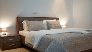 Een moderne slaapkamer met een houten hoofdbord, twee nachtkastjes met lampen, een bed met een grijs-wit gestreept beddegoed, en een klein ladeblokje.