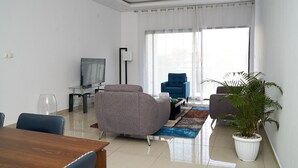 Een moderne woonkamer met een flatscreen televisie, grijze fauteuils, een salontafel en een potplant.