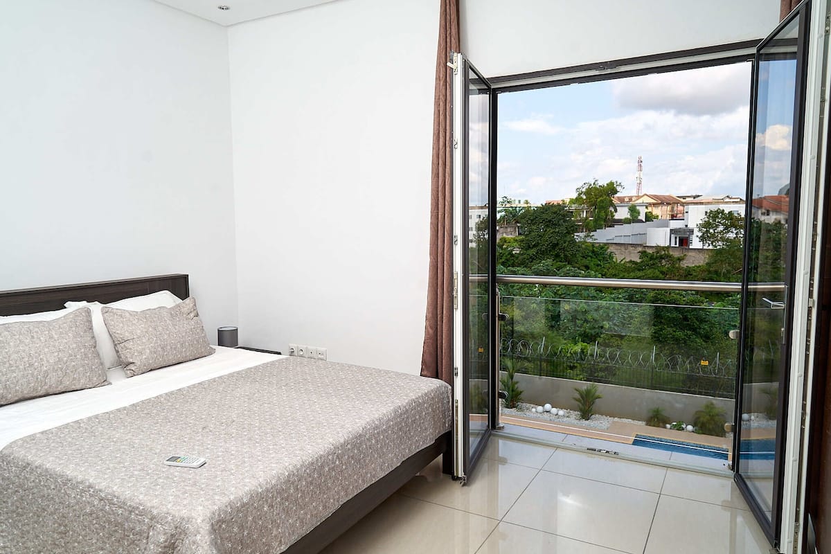 A bedroom with a bed, a nightstand, and a view through a glass door to an outdoor balcony.