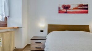Ein Schlafzimmer mit einem Bett, einem Nachttisch, einer Wandlampe, einer Heizung und einem Baumgemälde.