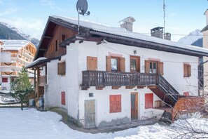 Un chalet traditionnel doté d’un balcon en bois, d’un escalier et d’un toit recouvert de neige.