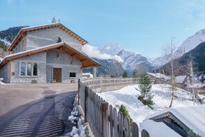 Ein Steinhaus mit Holzdach, einem Holzzaun und schneebedeckten Bergen im Hintergrund.