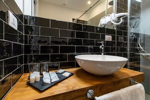 Un baño con un lavamanos grande de color blanco, paredes con azulejos negros y una encimera de madera.