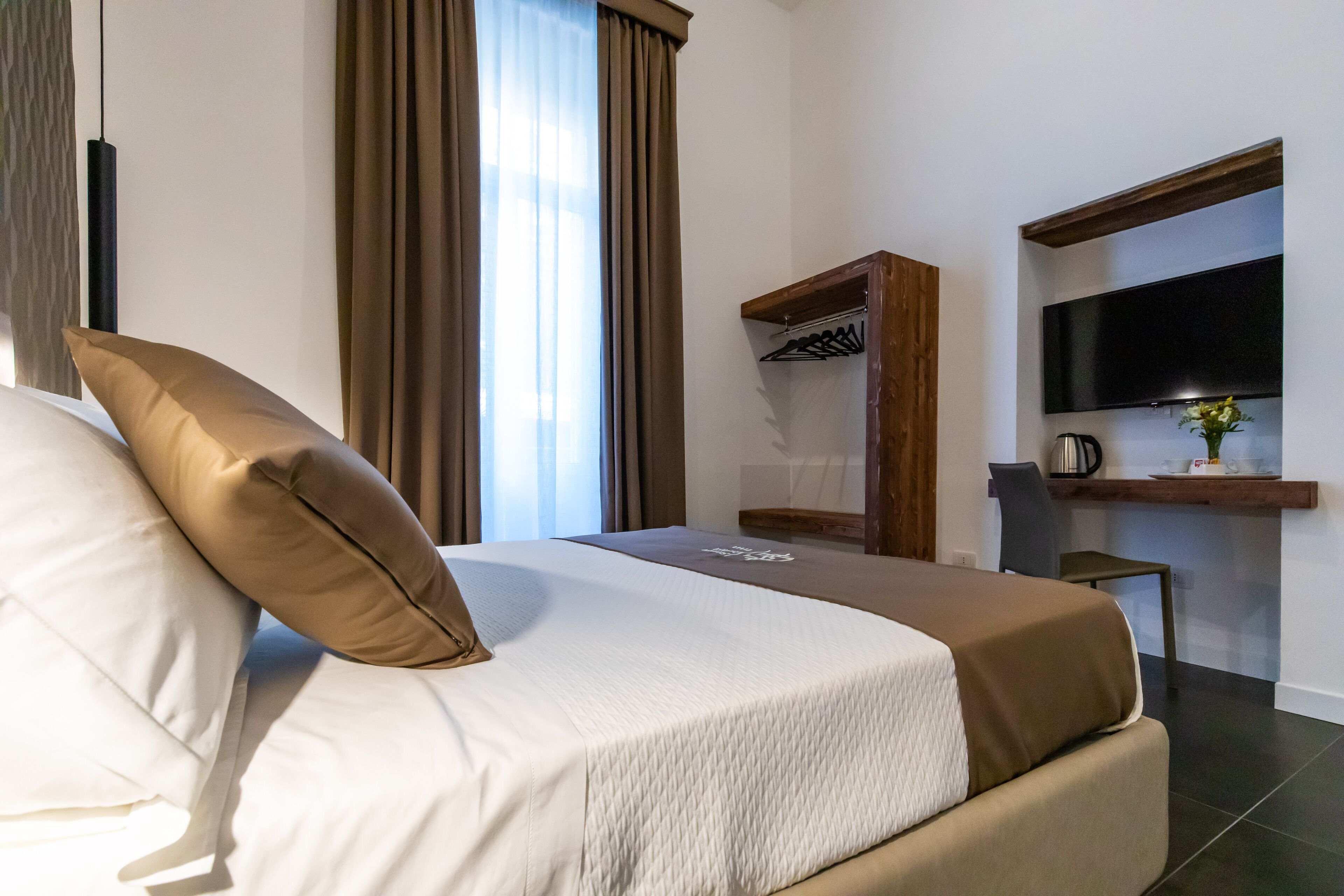 Ein Hotelzimmer mit Bett, Wandfernseher, Schreibtisch mit Stuhl und einem Vorhangfenster.