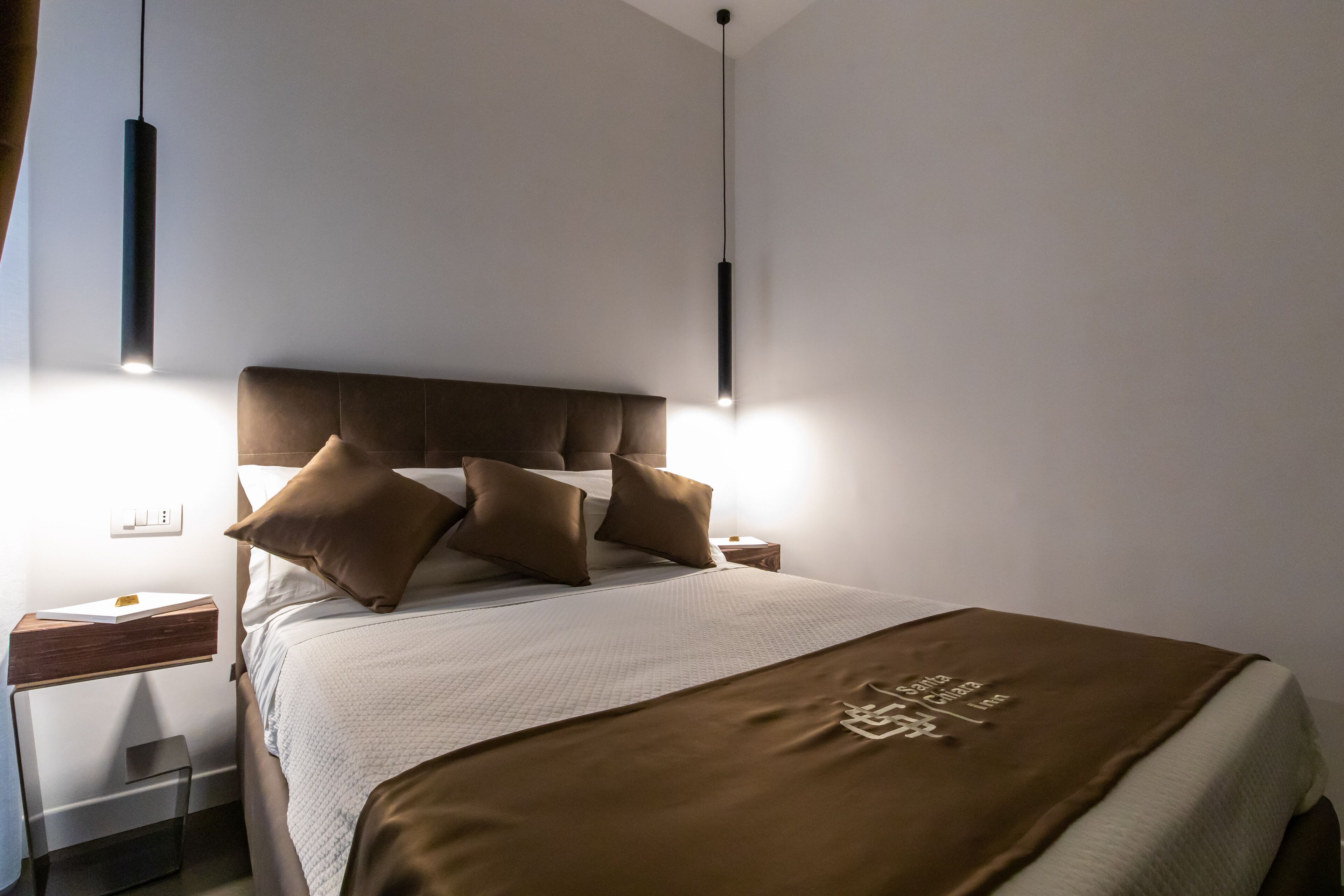 A modern hotel room with a large bed, two bedside tables, and pendant lighting.