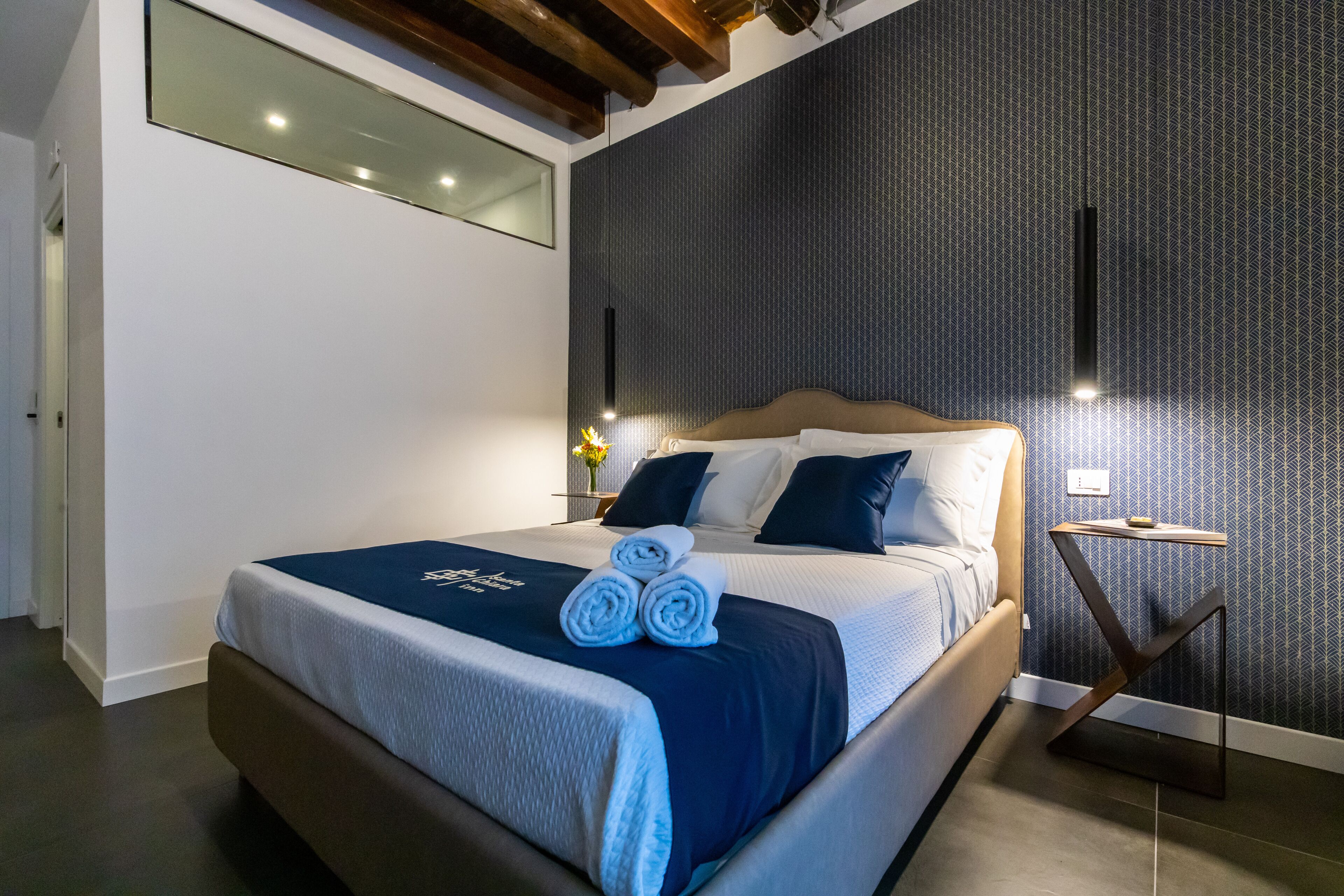 Una habitación de hotel moderna con una cama grande, una mesita de noche y una lámpara fijada a la pared.