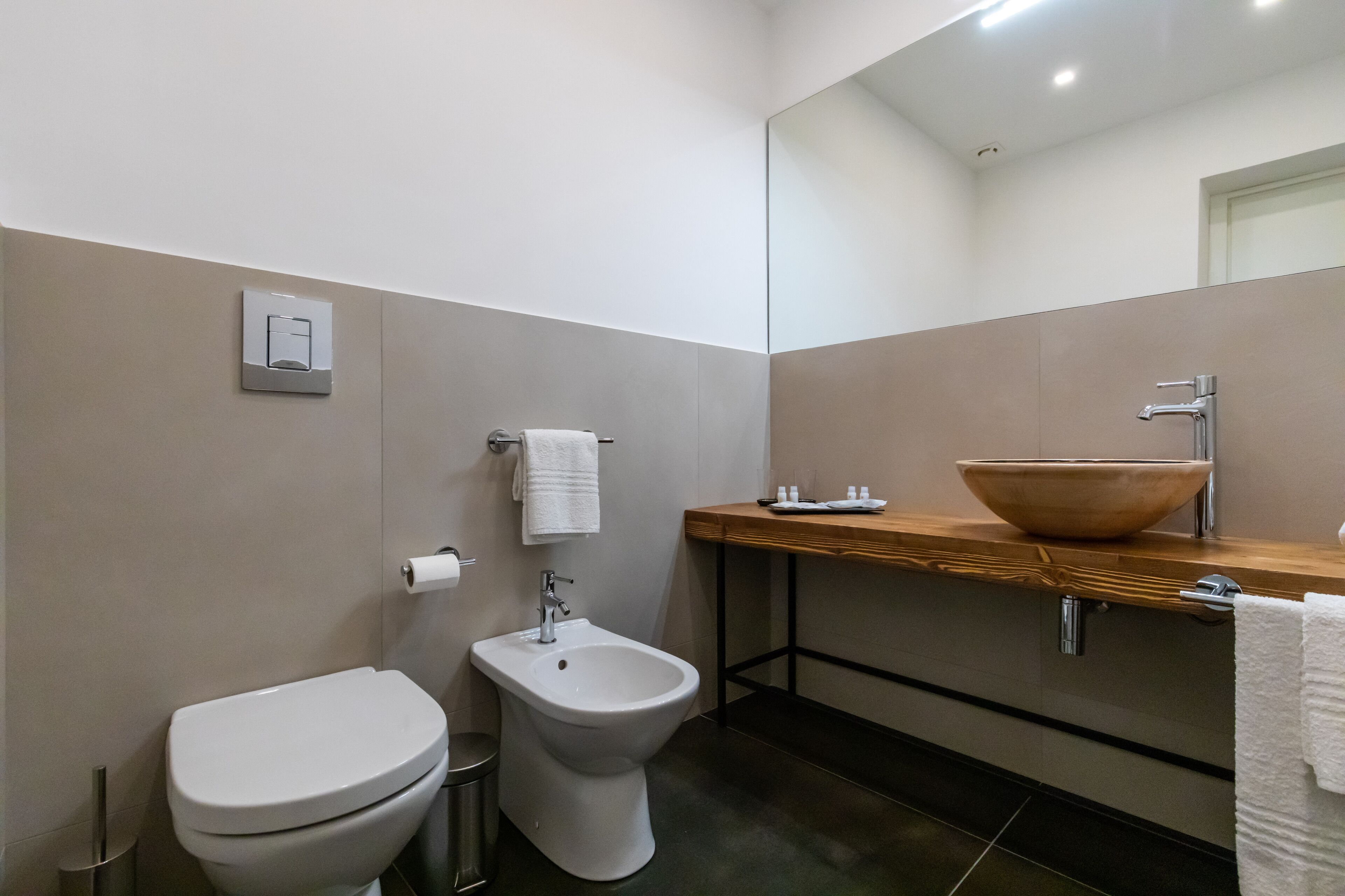 Un baño moderno con inodoro, bidé y tocador de madera con un lavamanos grande.