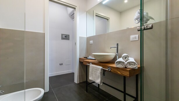 A modern bathroom with a white sink, a large mirror, and a glass shower enclosure. - Santa Chiara Inn (Naples)