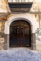 Fachada de un edificio con un amplio arco de entrada, una reja de metal y suelo de baldosas.