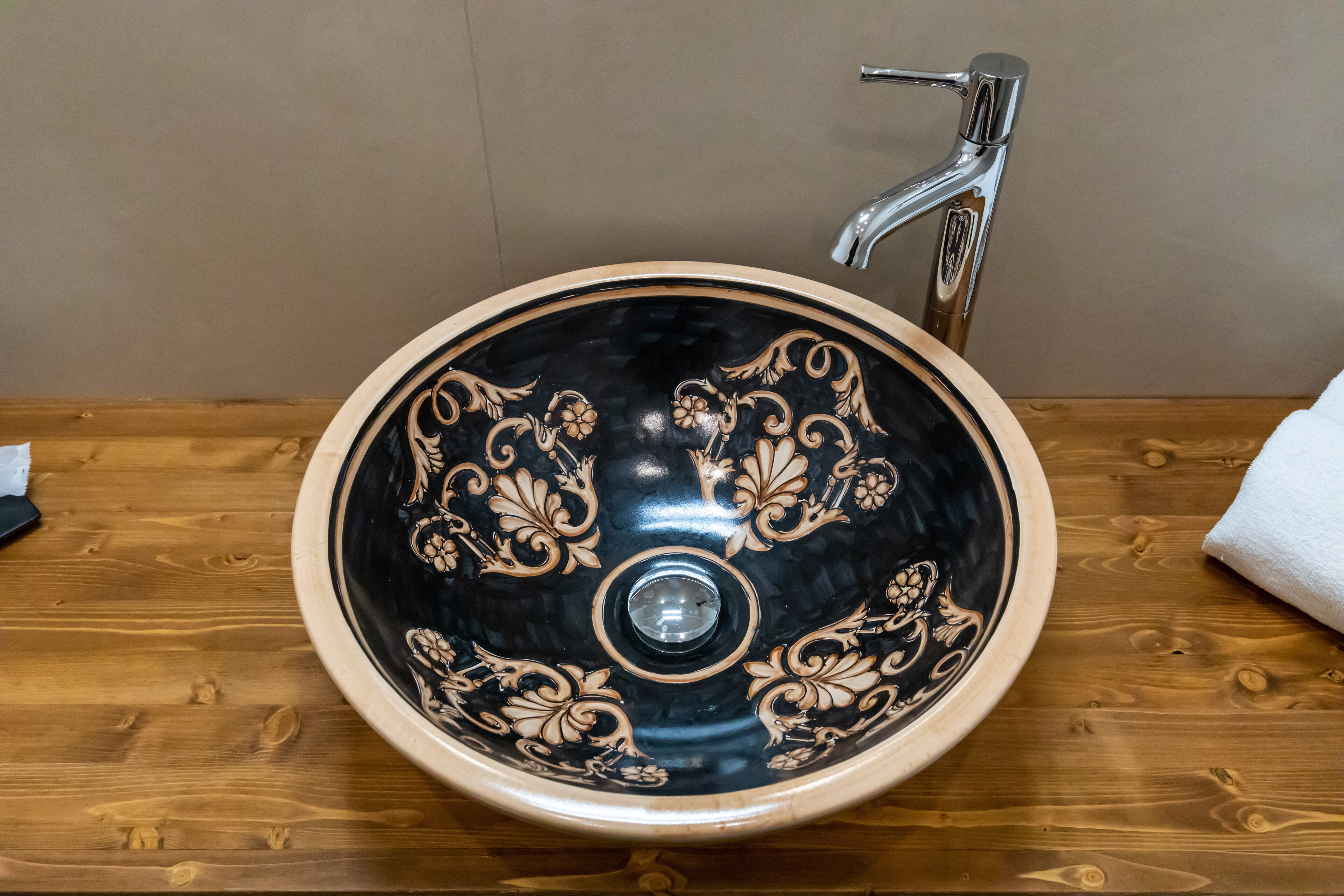 A black ceramic sink with ornate floral patterns, a chrome faucet, and a wooden countertop.