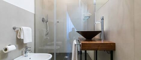 Un baño moderno con ducha de vidrio, tocador de madera, lavabo blanco y retrete.