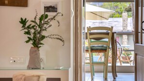 Une pièce avec une chaise en bois, une table en verre, une plante en pot et une vue à travers une porte vitrée.