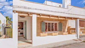 Un bâtiment blanc doté d’un porche abrité, d’une fenêtre avec des volets et d’un petit balcon agrémenté de jardinières.