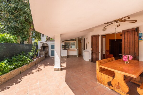 A covered patio with a wooden table and chairs, a ceiling fan, and a view of the garden.