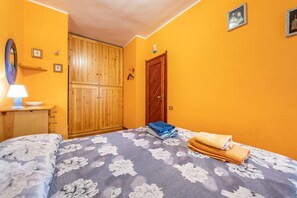 A bedroom with a bed, a wooden wardrobe, a nightstand with a lamp, and a wall with framed pictures.
