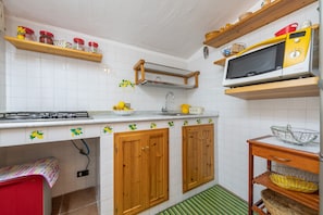 A kitchen with white tiled walls, wooden cabinets, a microwave, and a sink.
