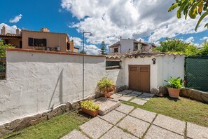 A courtyard with a paved walkway, potted plants, and a small wall.