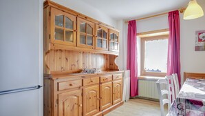 A kitchen with wooden cabinets, a dining table with chairs, and a window with curtains. - Spacious Apartment “Cesa Crepaz” with Mountain View, Wi-Fi & Garden (Canazei)
