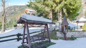 A wooden swing set with a snow-covered roof, a stone wall, and a small wooden structure with a conical roof. - Spacious Apartment “Cesa Crepaz” with Mountain View, Wi-Fi & Garden (Canazei)