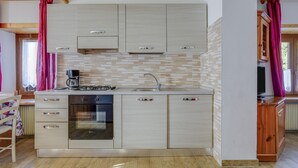 A compact kitchen with a gas stove, oven, and a coffee maker. - Spacious Apartment “Cesa Crepaz” with Mountain View, Wi-Fi & Garden (Canazei)