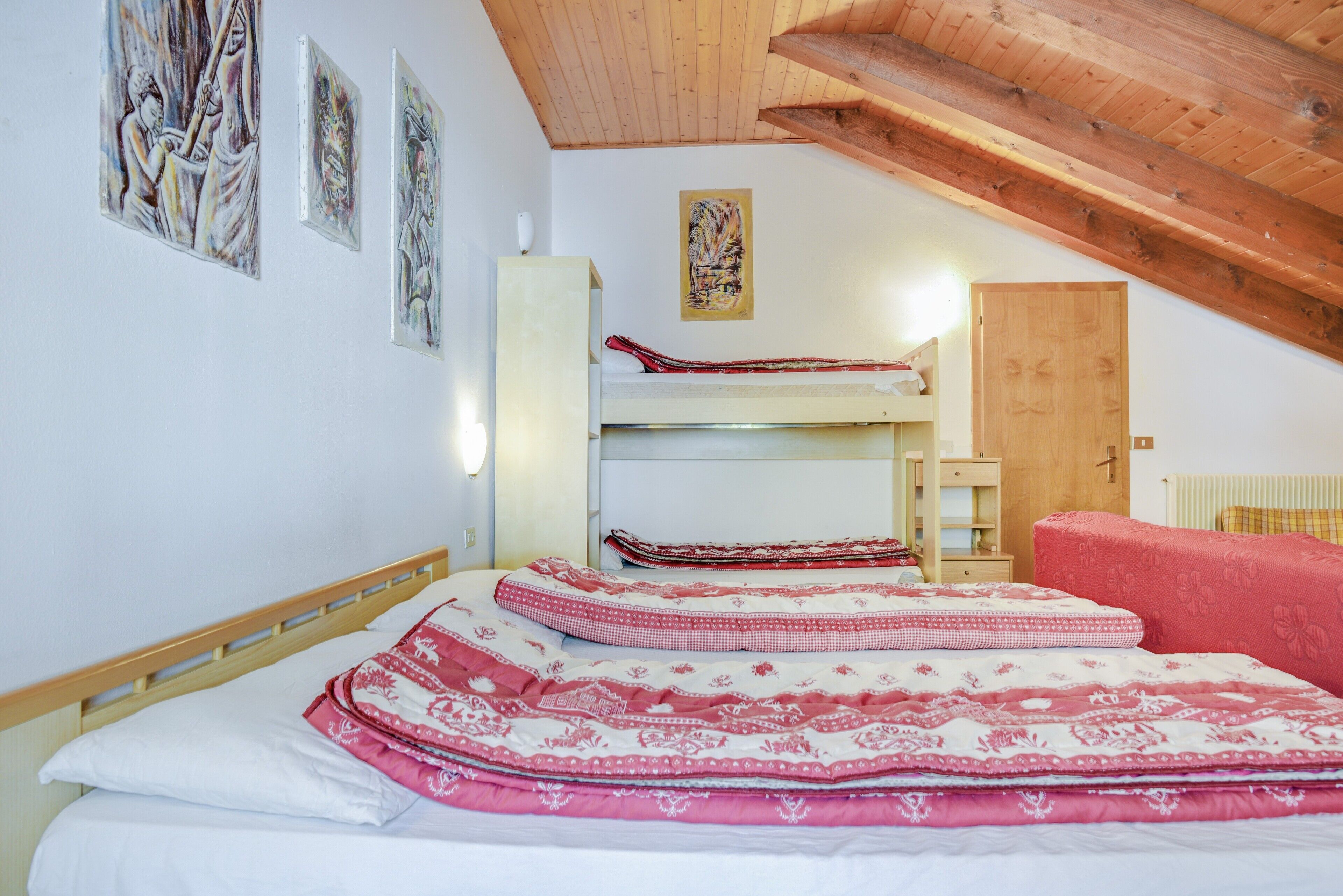 Una habitación con literas, techo de madera y obras de arte en las paredes.