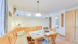 Une pièce avec un banc en bois, une table recouverte d’une nappe, un luminaire suspendu et une porte en bois.