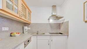 Une cuisine avec des meubles blancs, une hotte de cuisinière en acier inoxydable, une machine à café et un panier à fruits.