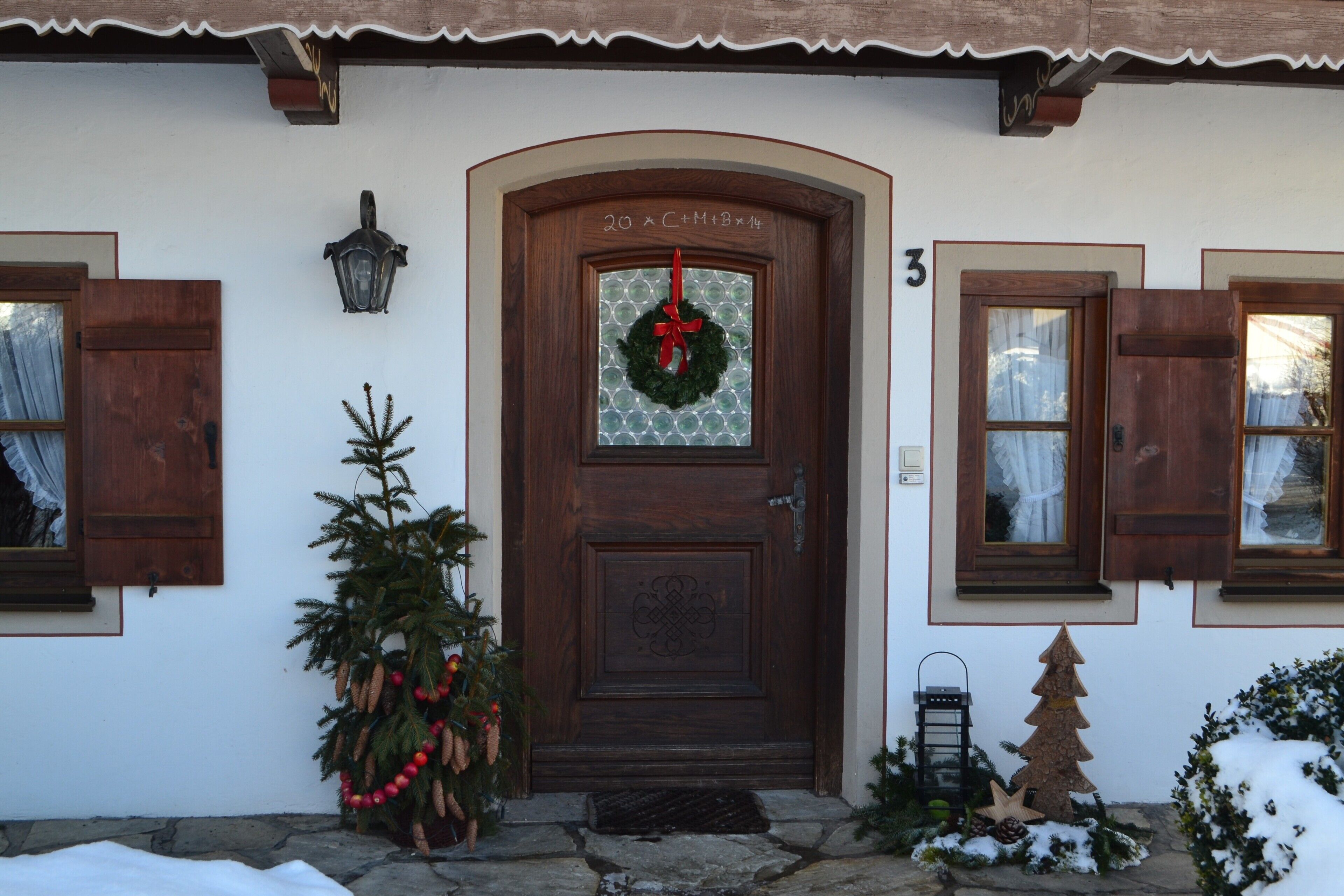 A wooden door with a wreath, a Christmas tree, and a snow-covered ground.
