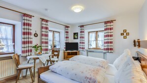 Une chambre à coucher avec un lit, deux chaises, un bureau, une télévision et des rideaux.