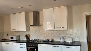 A modern kitchen with white cabinets, a microwave, a gas stove, and a coffee maker. - Luxurious Modern One Bedroom Apartment (Redhill)