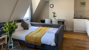 A modern bedroom with a bed, bedside table, and a small desk area. - Luxurious Modern One Bedroom Apartment (Redhill)