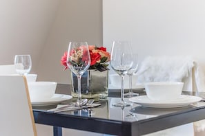 A dining table set with white plates, clear wine glasses, and a vase with red and pink flowers.