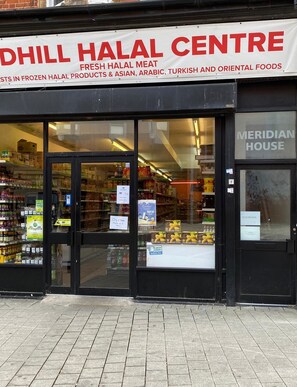 Fachada com uma placa indicando "Dhill Halal Centre", oferecendo carne halal fresca e produtos halal congelados.