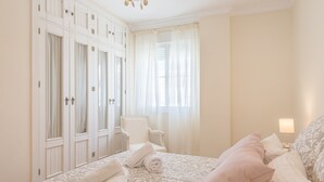 Ein Schlafzimmer mit einem Bett, einem Sessel, einem Kleiderschrank und einem Fenster mit Vorhängen.