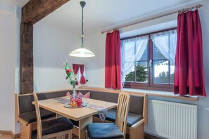 Uma área de refeições com mesa de madeira, bancos acolchoados, luminária pendente e janela com cortinas vermelhas.