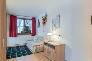 Um quarto com janela, radiador, sofá, armário e luminária.
