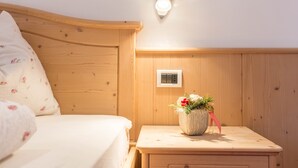 A wooden bed with a headboard, a bedside table with a vase of flowers, and a wall-mounted light fixture. - Holiday Apartment "Christa B1" with Wi-Fi near Various Ski Resorts (Ortisei)