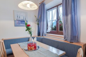 A dining area with a table set for four, a vase with flowers, and a window with curtains.