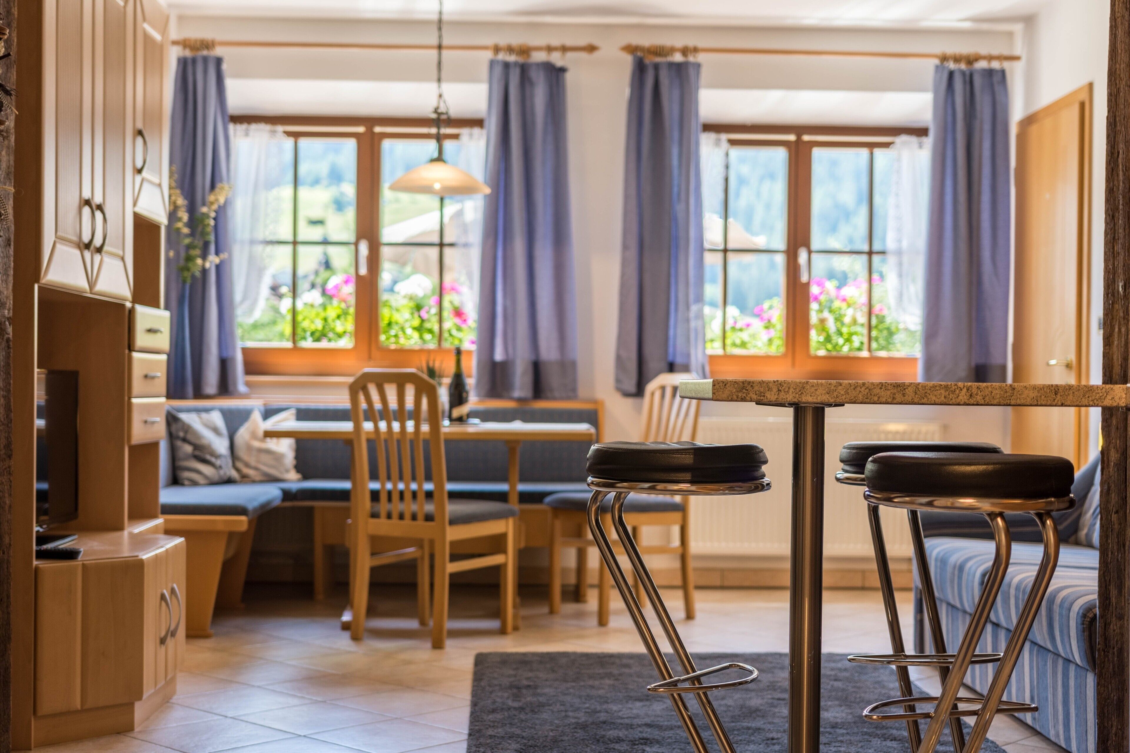 Une cuisine moderne avec un coin repas, des meubles en bois et de grandes fenêtres avec des rideaux.
