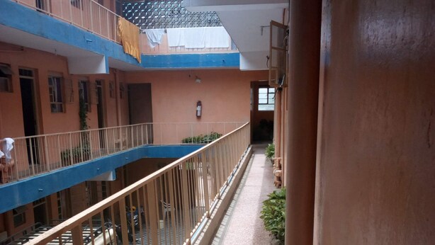 A corridor with a blue railing, a water tank, and a building with balconies. - Mocharo Hotel (Isiolo)