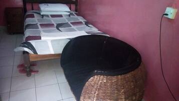 Une chambre à coucher avec un lit, une table de chevet, une prise électrique et un sol carrelé.