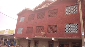 A multi-story building with a red brick facade, multiple windows with decorative grills, and a black SUV parked in front. - Mocharo Hotel (Isiolo)